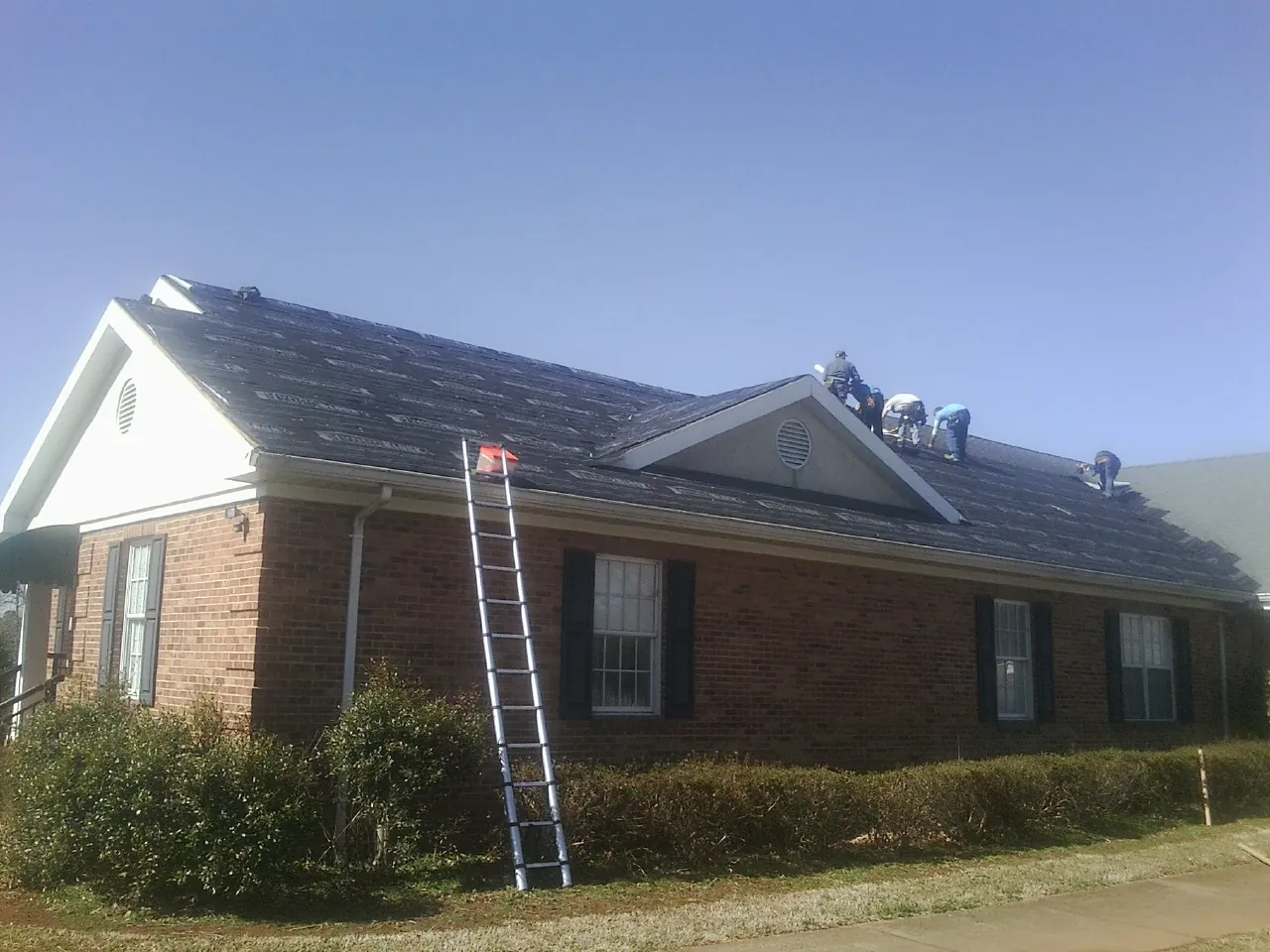 Crew tearing shingles off a brick ranch roof with a ladder set — Emergency Roof Repair work by our crew in Hodgenville