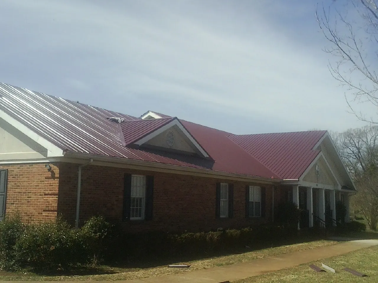 Red metal roof with gabled entries on a long brick building, from a Hail Damage Roof Repair job in Hodgenville