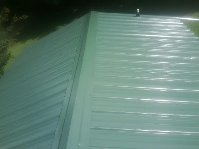 New green metal panels meeting at the ridge of a roof — Flat Roof Repair work by our crew in Hodgenville