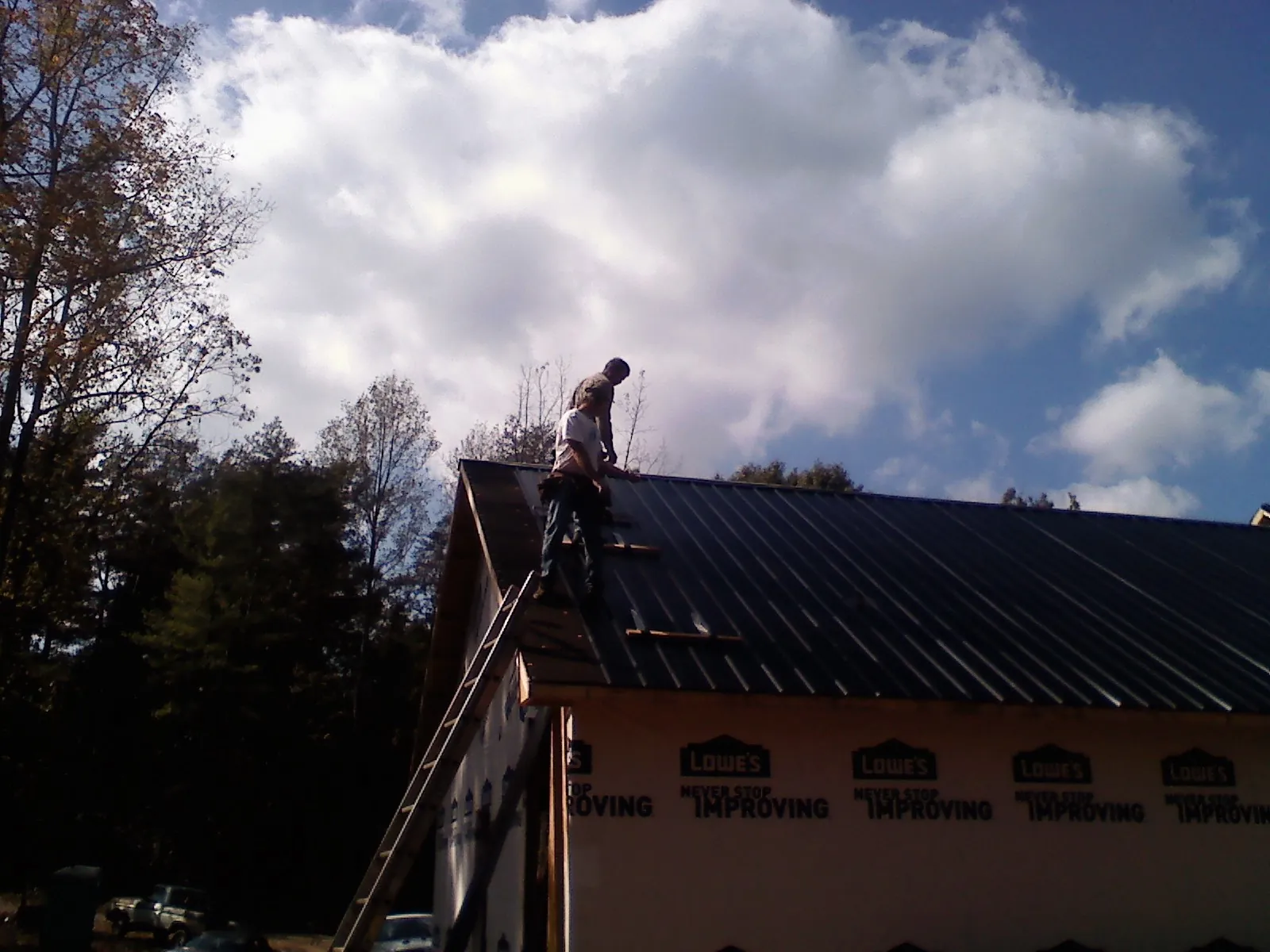 Roofer fastening dark metal panels high against a cloudy sky, from a Roof Inspection job in Hodgenville