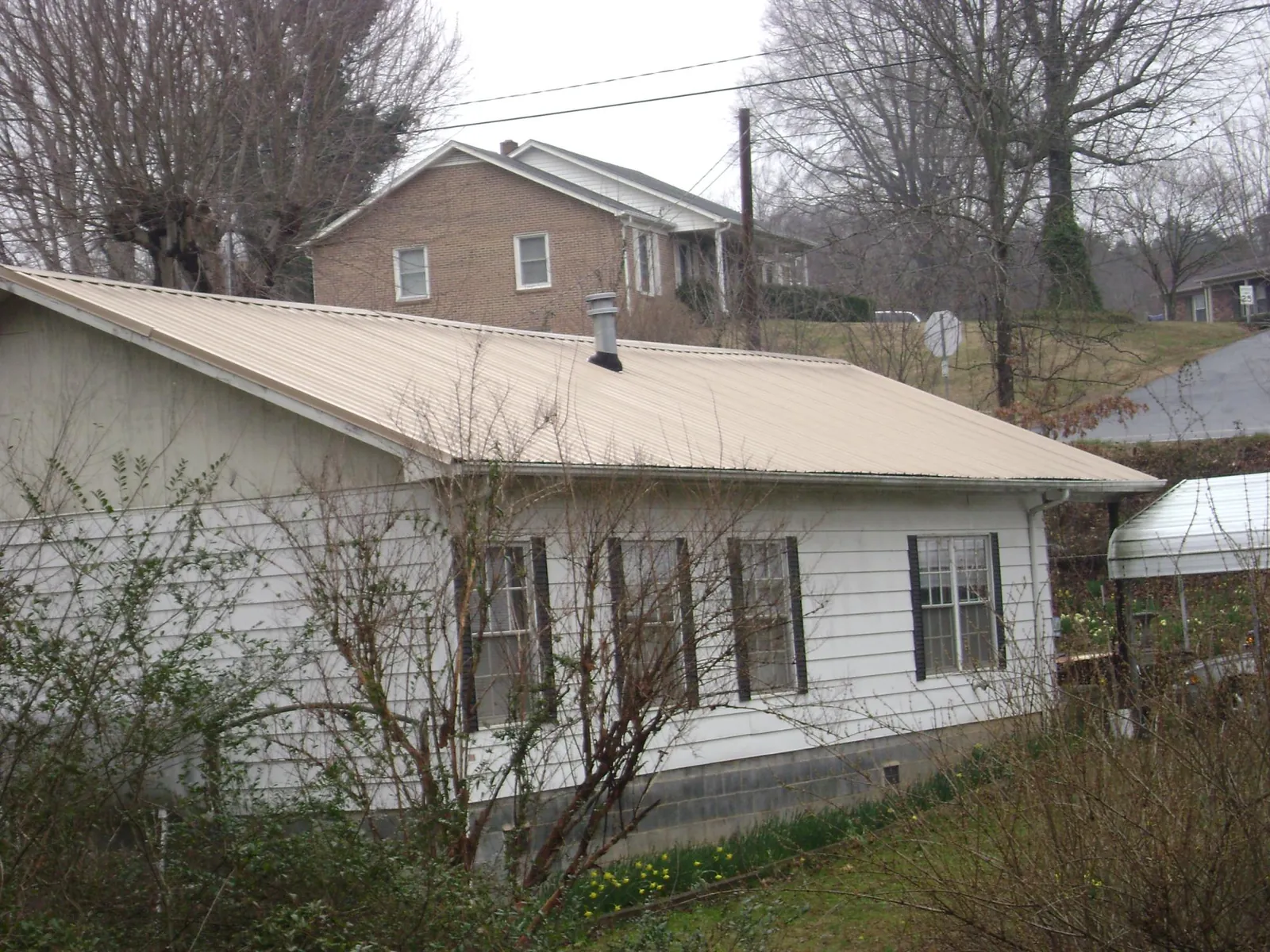 Tan metal roof on a white sided house set into a hillside — Commercial Roofing by Roofing Brothers in Hodgenville