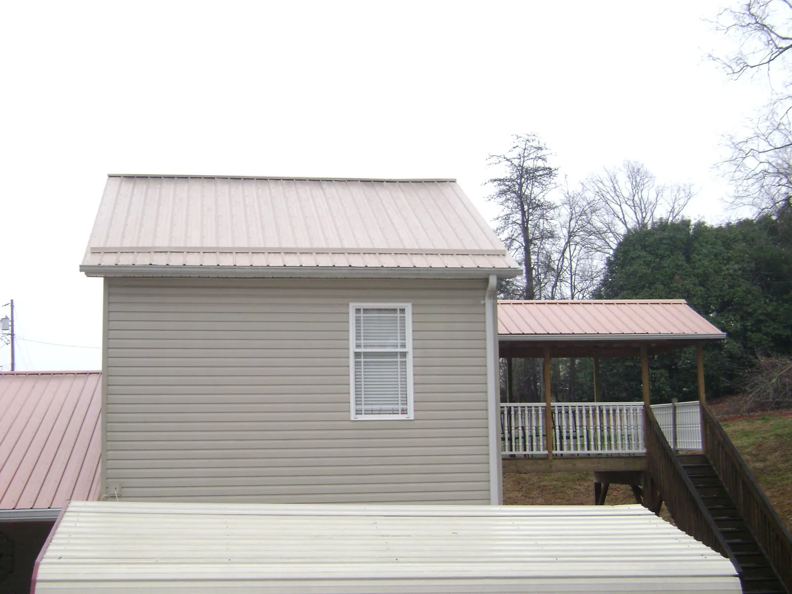 Tan metal roofs on a two story addition and attached porch, from a Roof Replacement job in Hodgenville